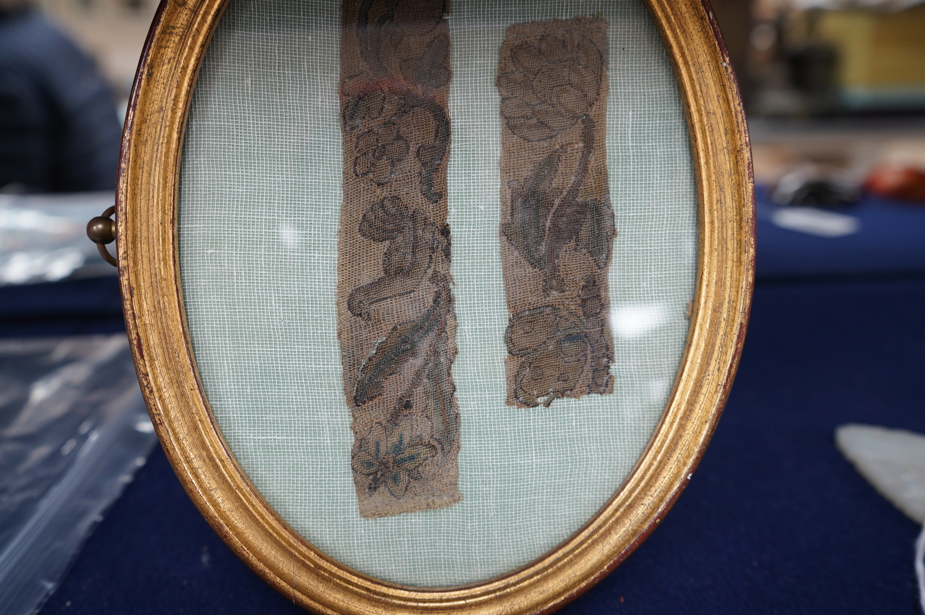 Two 17th century finely embroidered needlework fragments, possibly originally part of a casket or sampler, depicting a butterfly and flower on one and a bird and fruit on the other, in an oval gilt frame, largest fragmen